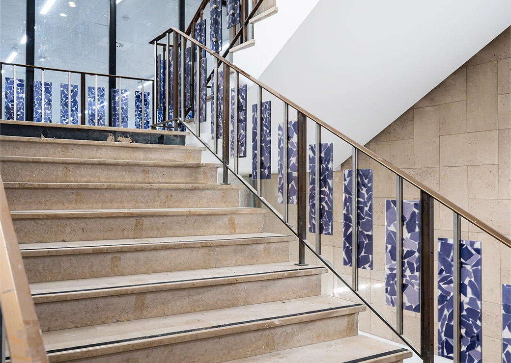 Vue de l'escalier, marches en marbre et panneaux décoratifs de mosaïque bleue sur la rampe.